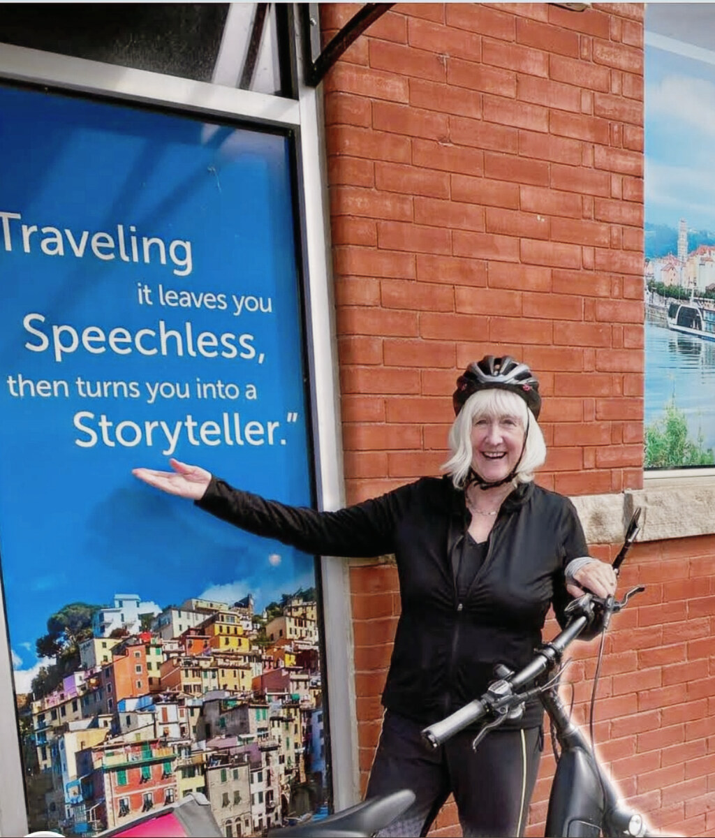 Smiling traveller standing with her bicycle beside a colourful travel poster